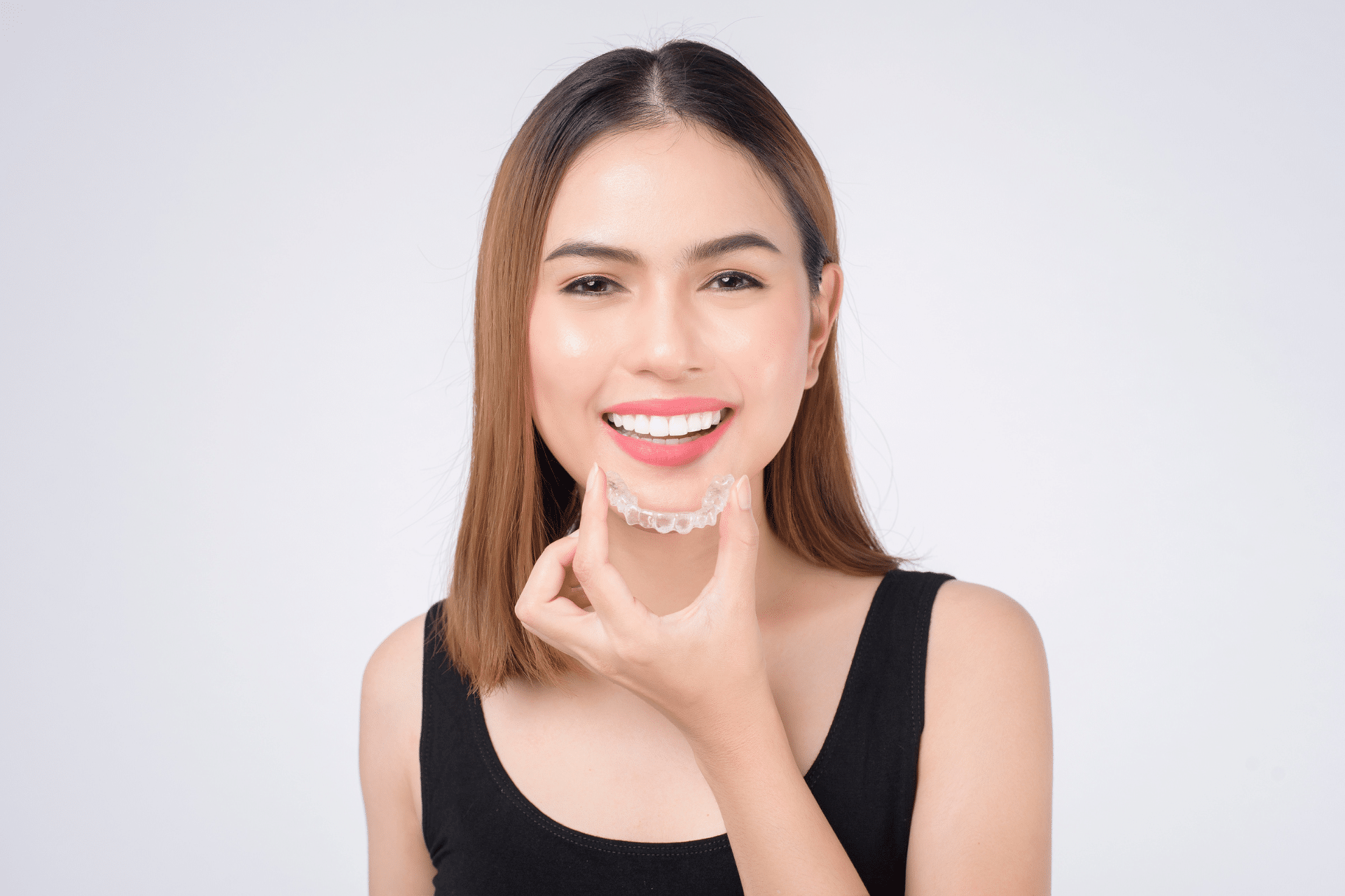 Woman holding clear aligner near chin | Nudera Orthodontics