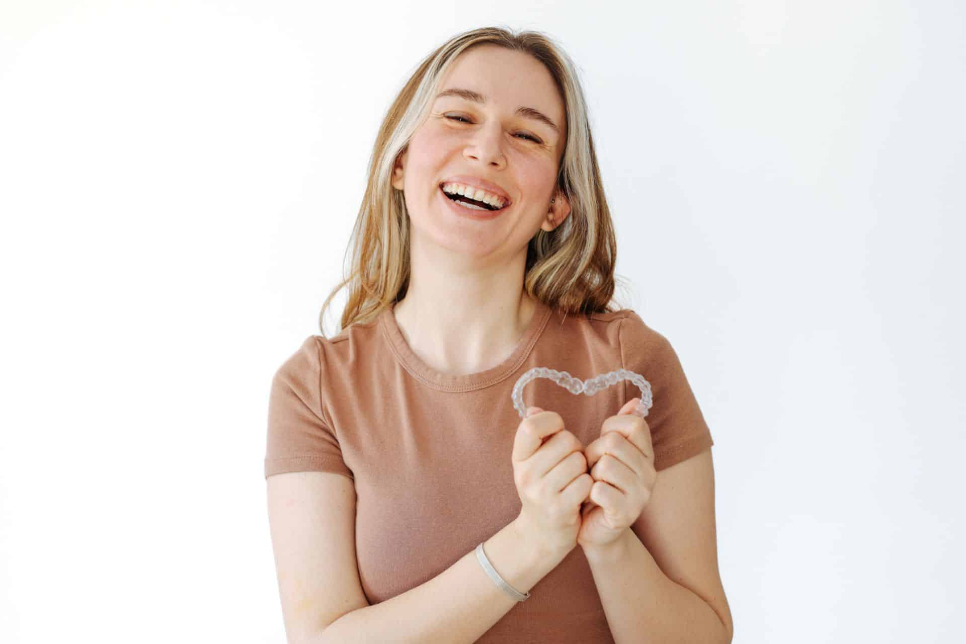 Woman laughing while holding heart shape | Nudera Orthodontics