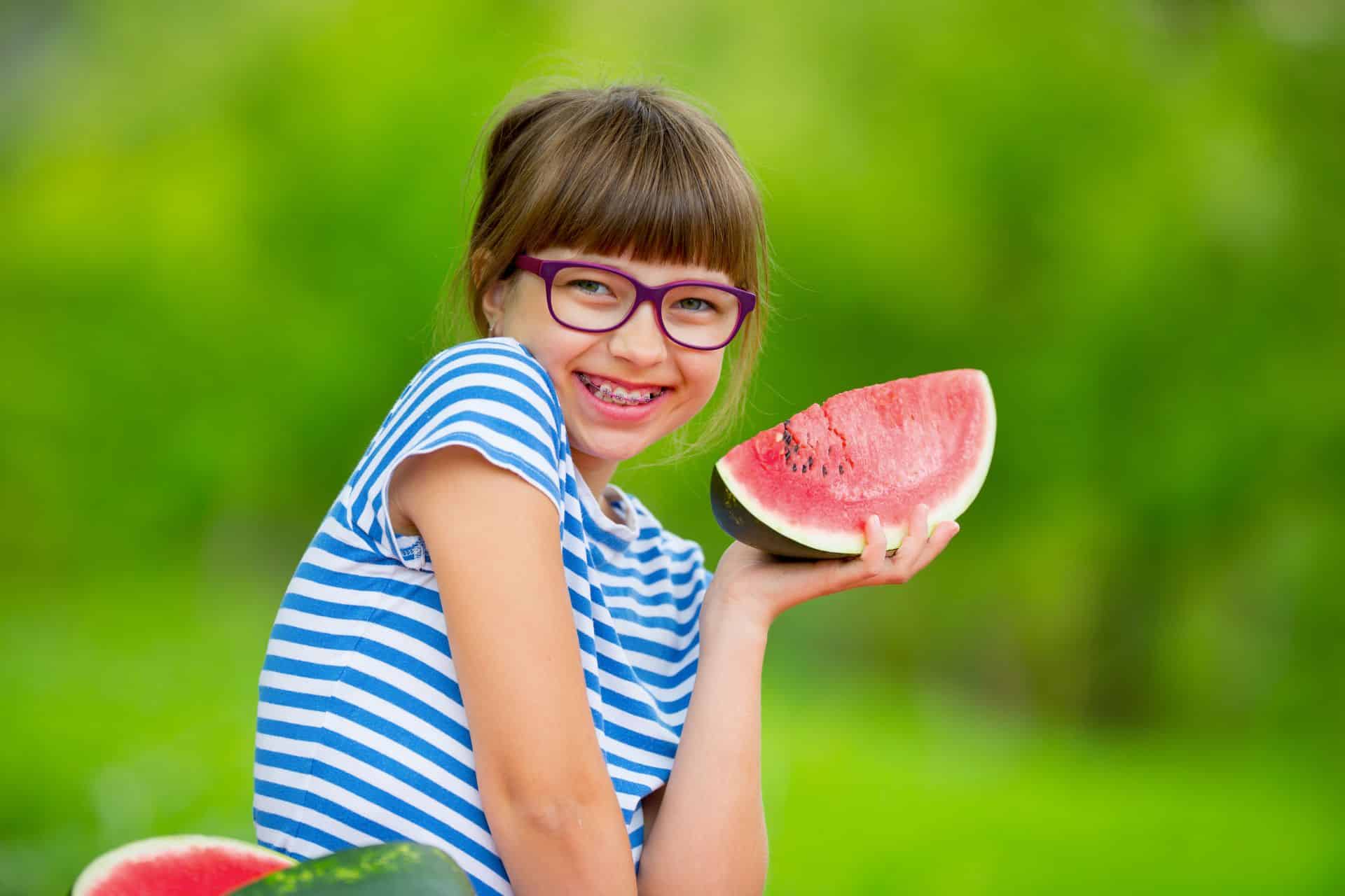 Young girl with glasses eating watermelon | Nudera Orthodontics