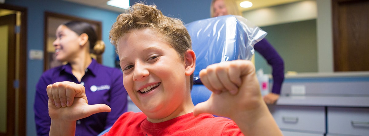 Boy flexing arm in dental chair | Nudera Orthodontics